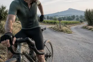 Tired cyclist pausing at a rural crossroads and putting a phone away before continuing.